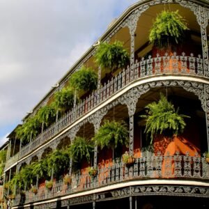 Detailed view of ornate ironwork balconies with lush greenery in New Orleans under a vibrant sky.