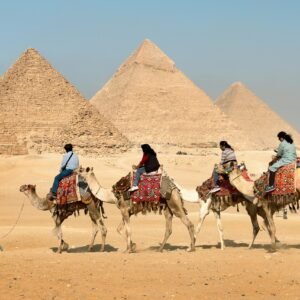 Tourists riding camels near the Great Pyramids of Giza, Egypt under clear skies.